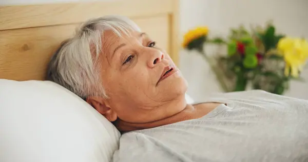 Depression, tired and an elderly woman in bed for peaceful rest or to relax in her retirement home closeup. Face, morning or insomnia with a senior person exhausted in the bedroom of an apartment.