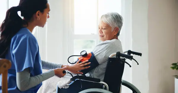 Woman, nurse and senior in wheelchair for blood pressure, monitoring or elderly care at old age home. Doctor or medical caregiver checking BPM of mature patient or person with a disability at house.