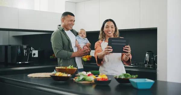 Family, tablet and selfie in kitchen, smile and internet on technology, cooking and memory. Happy parents and baby, profile picture and mobile app or cooking, digital and online or bonding in home.