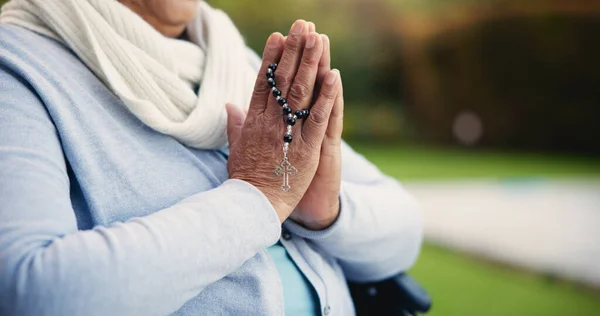 Senior, woman or hands praying with rosary for religion, worship and support for jesus christ in garden of home. Elderly, person and prayer beads for thank you, gratitude and trust in God for praise.