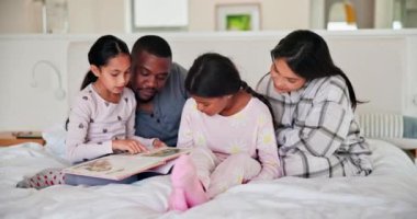 Ebeveynler, kız çocuklar ve kitap ile yatak, ırklar arası sevgi, ilgi ve bağlılık ile gülümseme ve okuma. Baba, anne ve kız çocukları yatak odasında güven, aile evinde dinleme ve hikaye.