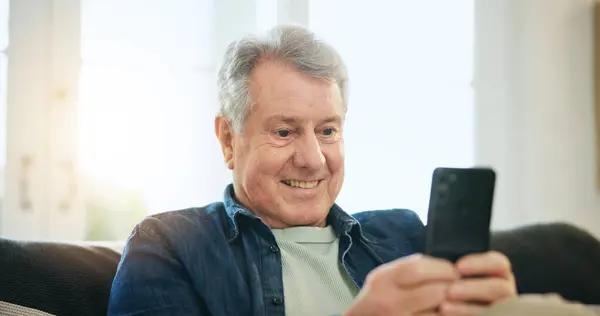 Happy senior man, phone and relax on sofa for communication, good news or networking at home. Mature male person smile on mobile smartphone for online chatting, texting or search on couch at house.