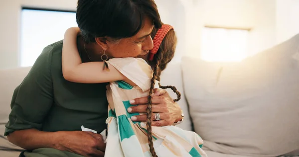 Family, love and girl hugging her grandmother on a sofa in the living room of their home during a visit together. Trust, care and security with a senior woman embracing her grandchild in an apartment.