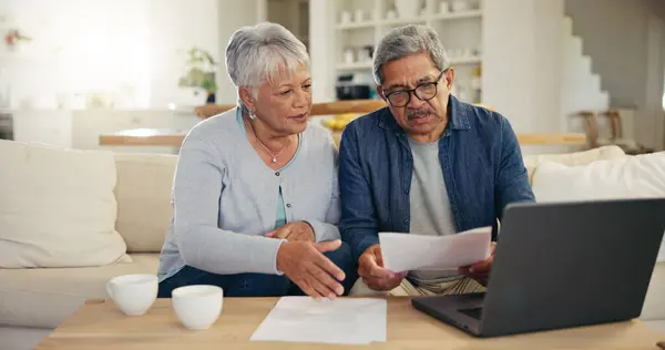 Elderly, couple and documents for financial planning in home with laptop, internet and reading for account balance. Senior man, woman and discussion with tech, webpage or online banking for budget.