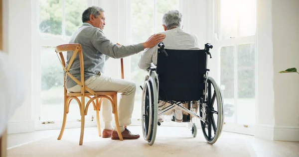 Elderly man, comfort and woman in wheelchair, touch and support partner in retirement with love. Senior couple, care and hand for together in marriage, sickness and health for wellness in family home.