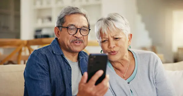 Senior couple, smartphone and video call in living room sofa, conversation and joyful. Grandparents, technology and communication with family, man and woman in retirement, happy and connection.
