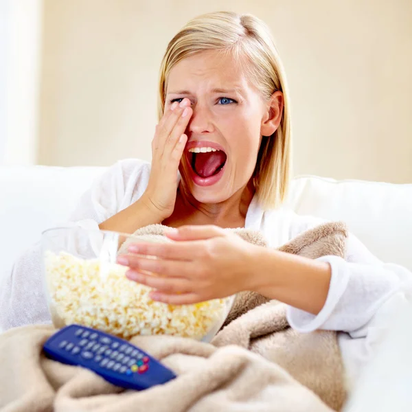 Horror, popcorn and woman on sofa watching tv with remote, blanket and streaming movies in home. Terror, television and girl on couch in living room with fear for scary video, film or network show