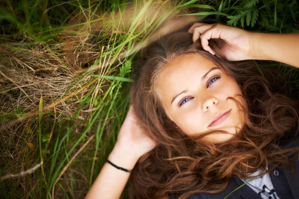 Serious, portrait and woman relax on grass in nature, countryside or field in environment. Calm, face and person lying on lawn in backyard, garden or meadow with freedom outdoor in spring or summer.