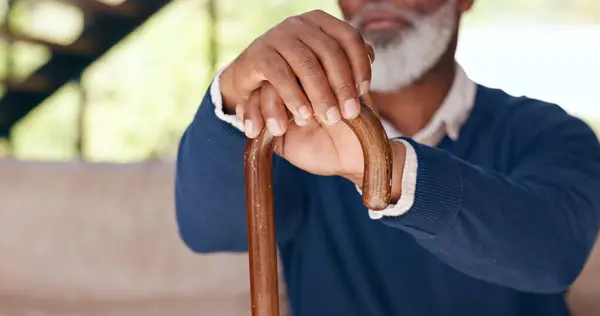 Hands, walking stick and a senior man on a sofa in the living room of his home for nostalgia closeup. Balance, cane or mobility aid and an elderly person with a disability in his apartment to relax.