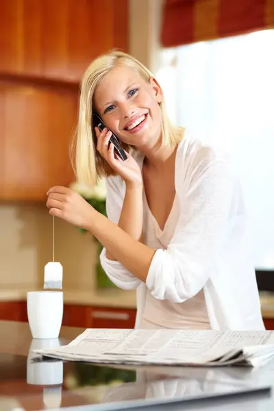 Woman, smile and phone call in kitchen, communication and newspaper or information at home. Female person, smartphone and conversation or chat, tea and hot drink for breaking news or laugh for joke.