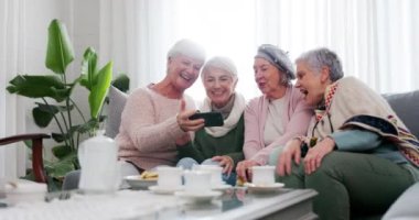 Telefon, sosyal medya ve üst düzey bayan arkadaşlar birlikte çay partisi için bir evin oturma odasında. Gülümse, emeklilik ve bir grup yaşlı insan bir mime gülerken birlikte kanepede oturuyor..