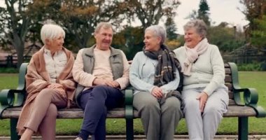 Sohbet, kaynaşma ve parkta kıdemli arkadaşlar birlikte temiz hava almak için bankta oturuyorlar. Mutlu, gülümseyen ve emeklilikte olan bir grup yaşlı insan açık yeşil bir bahçede konuşuyorlar.