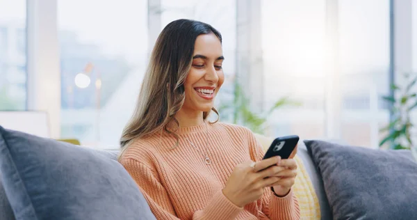 Woman, living room sofa and texting with phone, smile and click for contact, meme and notification in home. Girl, smartphone and happy with click, reading and app for social media, video and relax.