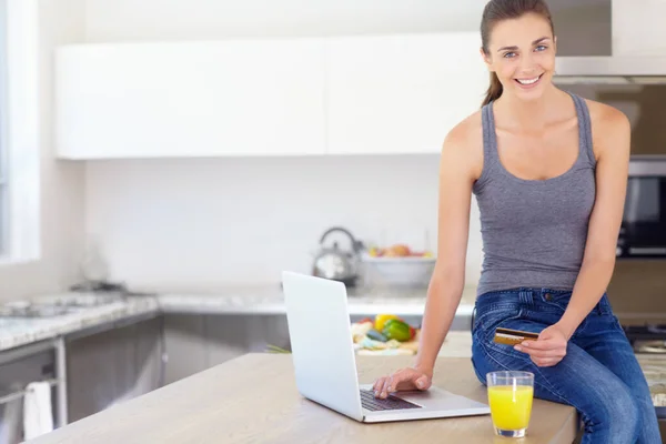 Portrait, credit card and laptop for online shopping with a woman in kitchen with orange juice in her home. Computer, smile or ecommerce with a happy young person in her apartment for finance payment.