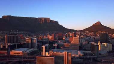 Hava aracı, dağ ve Cape Town şehrinde endüstriyel mimarisi ve mavi gökyüzü olan binalar. Gün batımında kasaba, altyapı veya açık şehir alanı, banliyö veya şehir manzarası görüntüsü.
