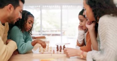 Aile, çocuklar ve ebeveynler oyun öğretirken veya öğrenirken evde satranç oynuyorlar. Çok ırklı erkek, kadın ve çocuklar eğlence, gelişme ya da masada kaynaşma yarışması için birlikte oynuyorlar..