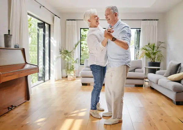 Love, dance and a senior couple in the living room of their home together for retirement bonding. Smile, trust or holding hands with an elderly man and woman moving in their apartment for romance.