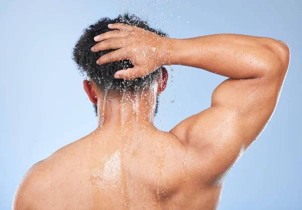 Man, shower back and hair care in studio with water splash, hygiene or muscle by blue background. Person, guy and cleaning with drop, wellness and health for skin, natural and dermatology for body.