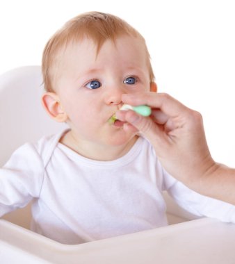 Şirin, kaşık ve bebek sağlıklı beslenmek için bir stüdyoda beslenme koltuğunda sebze yiyor. Tatlı, doğal ve yeni doğmuş çocuk, çocuk ya da çocuk beyaz arka planda sağlıklı beslenmenin tadını çıkarıyor.