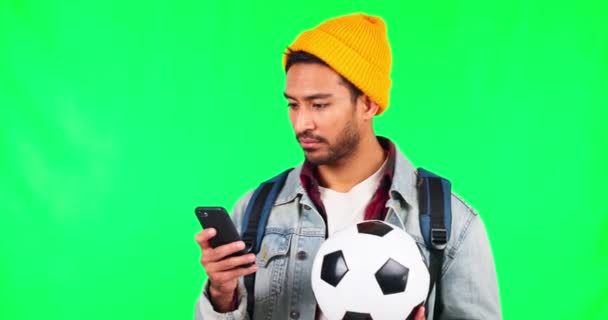 Young man, green screen and phone with football, texting and communication with reading in studio. Student guy, smartphone and soccer ball for sports gambling, betting and social media by background.