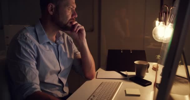 上班时间晚上 男人在电脑前思考和阅读邮件 网站或在线报告 为市场研究 延迟工作和建立关系网提供头脑风暴 问题解决和商人服务 — 图库视频影像