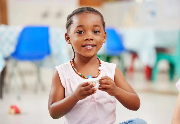 Portrait, little girl and cup with smile in kindergarten, daycare or classroom for playing. African kid, youth and happy for fun with delicious, fresh and beverage for development of motor skills.
