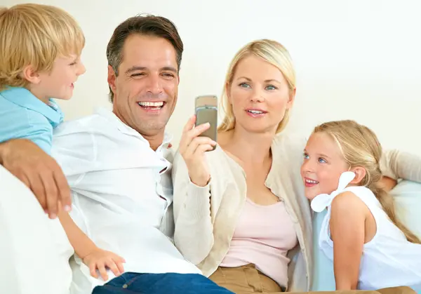 Family, face or happy on sofa with phone for social media, streaming or internet video with relax, peace and love. Parents, kids or smile with smartphone on couch of lounge with care or break in home.