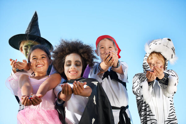 Children, group and hands in halloween costume for sweet candy asking, trick or treat for fantasy. Friends, smile and dress up as witch or pirate for holiday fun, kid development on sky background.
