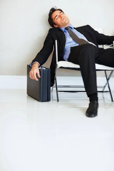 Business man, sleeping and case in lobby, chair and fatigue from travel, overworked or burnout in suit. Entrepreneur, briefcase and tired with rest, exhausted or luggage for corporate job with stress.