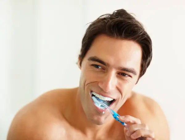 Bathroom, brushing teeth and man with oral health, wellness and grooming routine for fresh breath. Person, home or guy with toothbrush, cleaning his mouth and morning with dental hygiene or self care.
