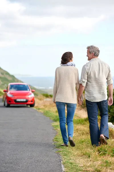 Old couple, walking and holding hands in nature on holiday, vacation or retirement with support. Back, man and woman with love, car and happiness in marriage together on a road trip or journey.