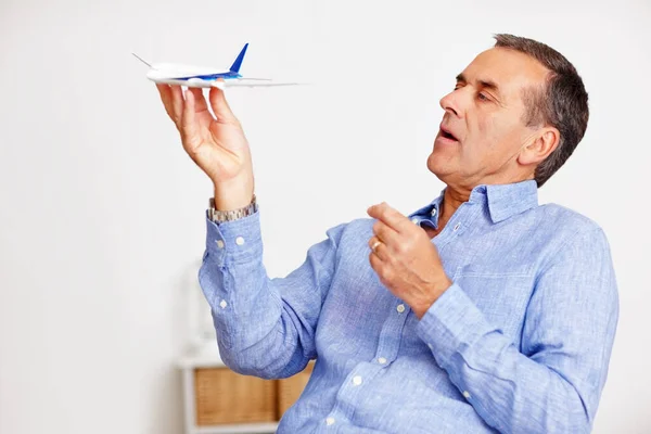 Mature man, flying and toy plane for travel, vacation and holiday planning with a smile at home. Happy, airplane model and retirement of a male person with confidence from trip and air traveling.