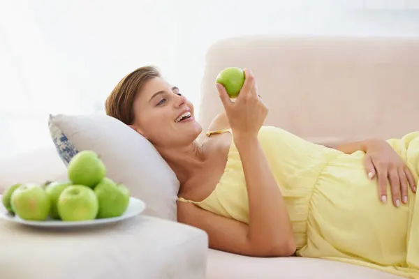 妊娠中の女性 リンゴ 笑顔で健康 アパートのリビングルームで健康 リラックス ビタミンと健康的な食事のためのラウンジのソファーで人 フルーツと幸せ — ストック写真