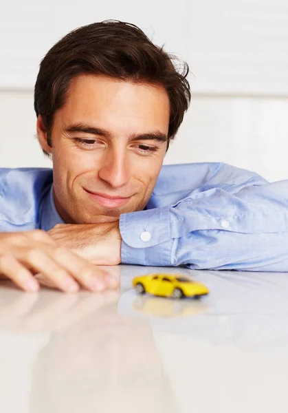 Toy car, business and man with a smile, office and employee with happiness, cheerful or entrepreneur. Person, agent or consultant playing with vehicle, break or relax with peace, professional or calm.