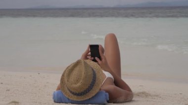 Plaj, tatil ve kadınlar telefonla, sosyal medyayla ve dalgalarla okyanusta bir yazı yazarak rahatlıyor. Yaz, tatil ve Endonezya 'da deniz, su ve tropik ada üzerinde akıllı telefonu olan kişi..