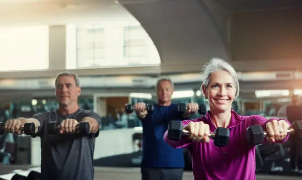 Senior fitness club, dumbbells and people at gym for training, health and wellness, sport or exercise. Class, workout and elderly group of friends at a studio for hand weight, cardio or weightlifting.