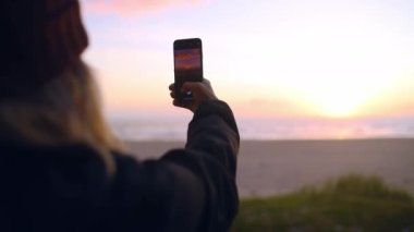 Sosyal medya, dijital hafıza ve seyahat blogu için kadın, telefon ekranı ve plaj ve gün batımı görüntüleri. Okyanus, deniz ve dalgaların video kaydı için cep telefonu kullanan mutlu genç ya da etkili kişi.