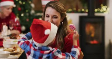 Mutlu çocuk, anne ve Noel 'de sevgi, ilgi ya da bağlılık için evde kucaklaşmak. Küçük çocuk ya da çocuk, hafta sonu evde tatil tatili için yemek masasında annesine şapka ve şekerle sarılıyor..
