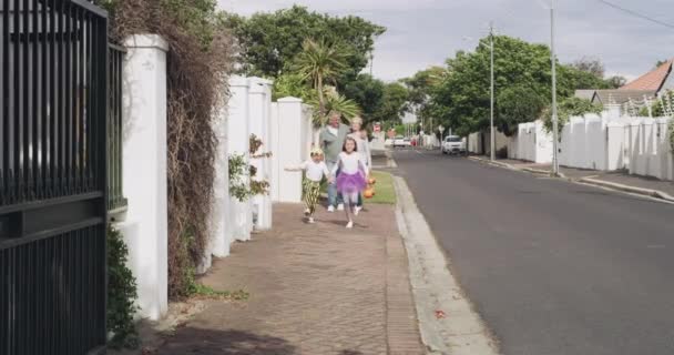 ハロウィーン 興奮と近所の通りで祖父母とコスチュームを着た子供たちは トリックや治療をします ホリデー シニアを持つ子供 姉妹が一緒に道を歩いている — ストック動画