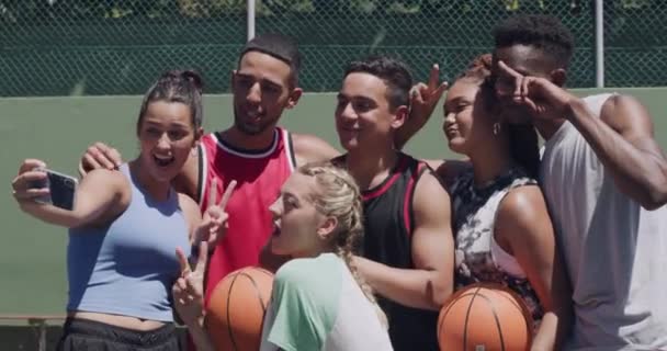 チームとセルフィー バスケットボールコート スマートフォン 女の子 男の子と幸せで笑顔 ソーシャルメディア スポーツ 平和サインのためのアスリートやゲーム — ストック動画
