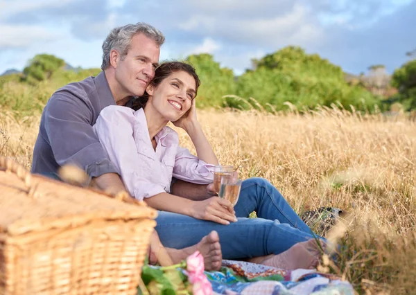 Senior couple, relax and picnic in park, grass and basket in nature for a date in retirement with love or care. Mature, woman and man in field in summer, holiday or vacation with freedom and drinks.