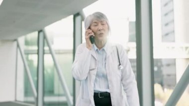 Telefon, tele sağlık ve kadın doktor koridorda yürürken cep telefonuyla konuşuyor. Teknoloji, kadın ve kıdemli Asyalı sağlık çalışanı cep telefonunda online tıbbi danışmanlık yapıyor..
