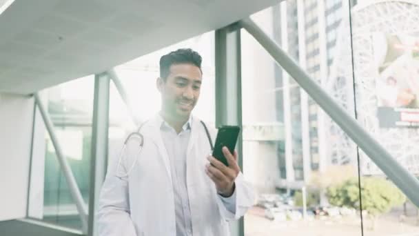 ビデオ通話 病院の医師が廊下を歩いている 携帯電話でオンライン医療相談を行うテクノロジー モバイル 若い男性医療従事者 — ストック動画