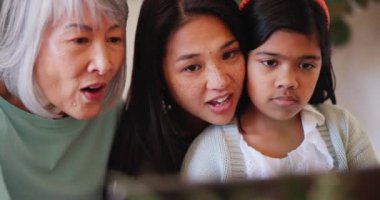 Yüz, tablet ve Asyalı bir aile öğrenme ve oyun oynamak için evlerinin oturma odasında bir arada. Anne, kız ve büyükanne sosyal medya, araştırma ve çocuk gelişimi için bir teknoloji uygulaması kullanıyor.