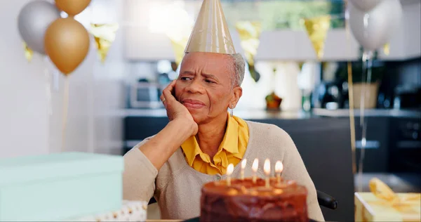 Sad, birthday and senior woman thinking with depression, grief and lonely in her home. Cake, face and elderly African person alone at a party with disappointment, frustrated or annoyed in a house.