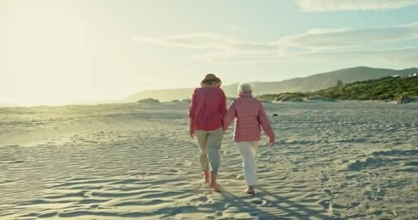 老年妇女 回来和休假在海滩上 结伴和在沙滩上散步或度假 年事已高的朋友 彼此相爱 手牵手为退休 聊天和外出旅行提供支持 — 图库视频影像