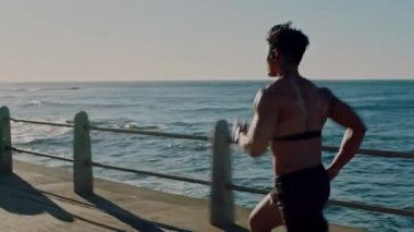 Koşucu, fitness ve plajda koşan adam, enerji dolu kardiyo ve hız, güçlü ve kalp monitörü. Kulaklıklar, podcast ya da motivasyon için müzik okyanus güneşi tarafından egzersiz ve açık hava sporları için kullanılıyor..