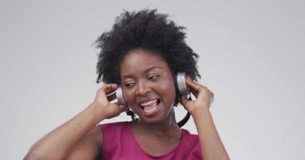 スタジオのダンス アフリカの女性は オーディオ ストリーミングソング ラジオを聴いています エネルギー サブスクリプション または灰色の背景で楽しいヘッドフォンと興奮する人の幸せな ダンスと肖像画 — ストック動画