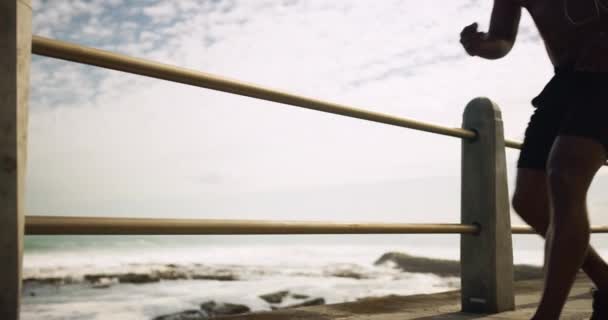 フィットネス 音楽を聴くための海洋遊歩道フェンスによるランナーマン 疲れたイヤホン アフリカの人 疲労とトレーニングと運動 ストリーミング購読のための思考や携帯電話 — ストック動画
