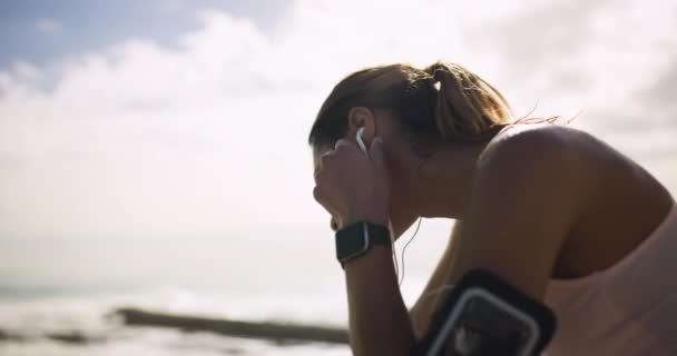 ランナーの女性 疲れた 海によるイヤホン 音楽を聴くヴィジョン オーディオストリーミングサブスクリプションのための疲労 電話で少女 トレーニングとエクササイズ — ストック動画